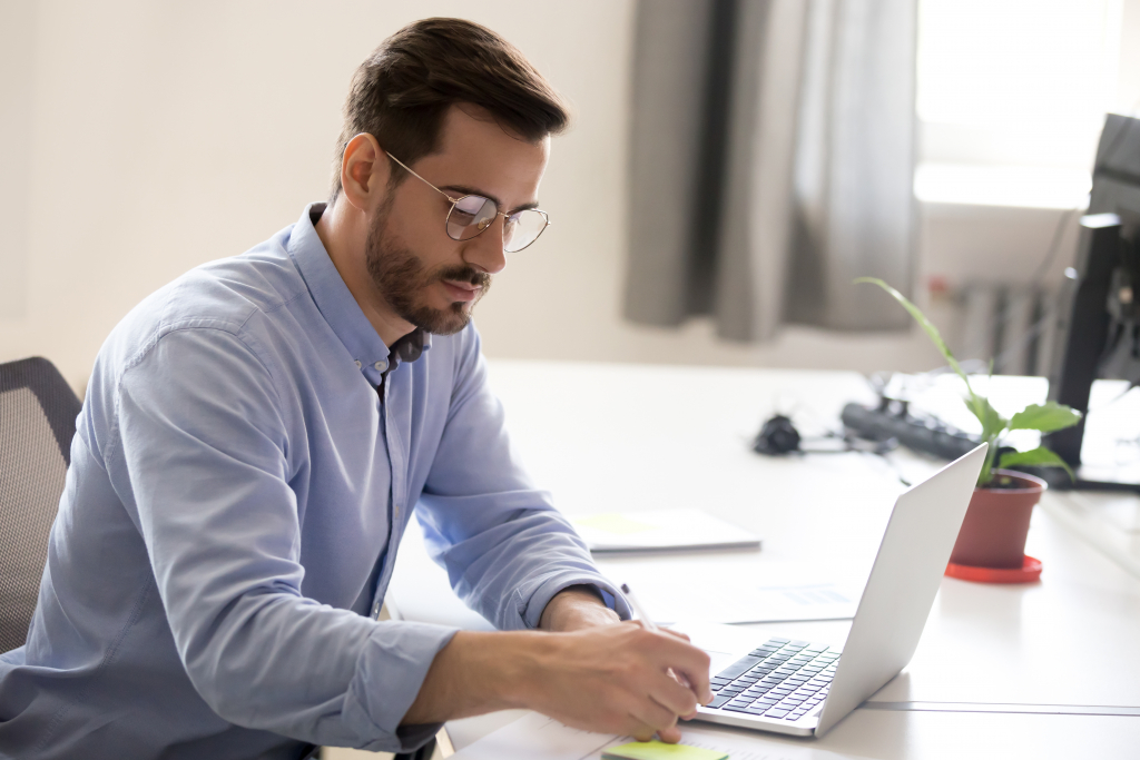 Homme prenant des notes devant un ordinateur portable