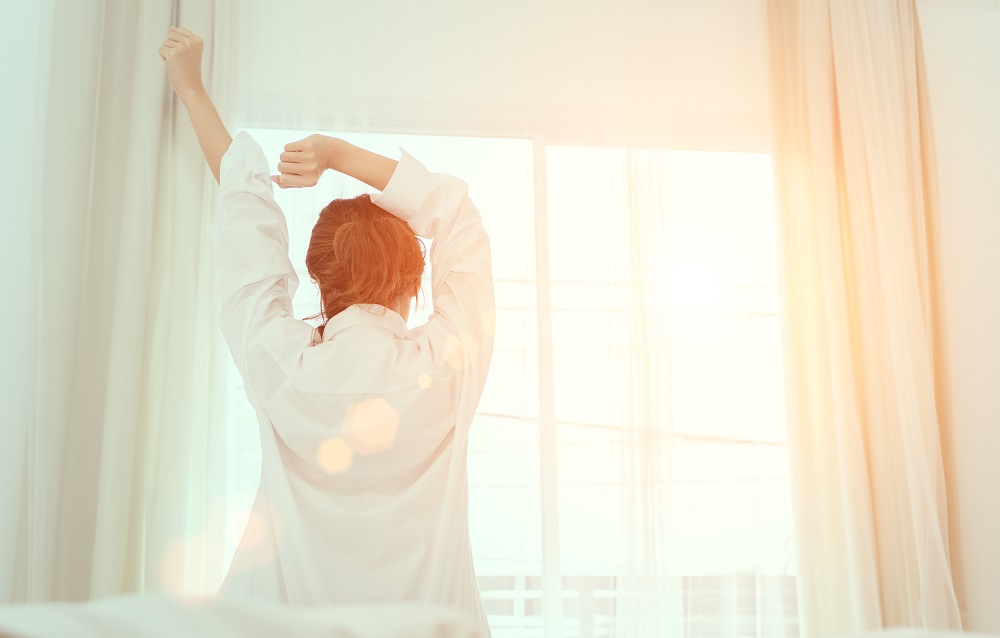 Femme en train de se réveiller le matin devant une fenêtre lumineuse. 