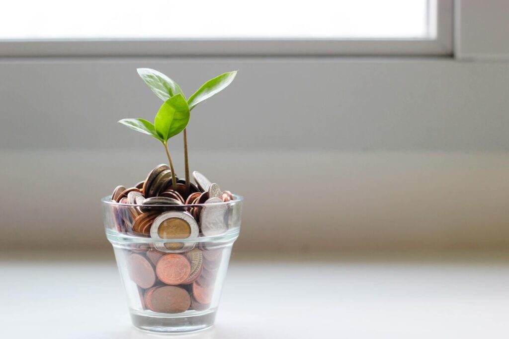 Des pièces de monnaie dans un verre et des petites pousses de plantes symbolisant l'énergie verte.
