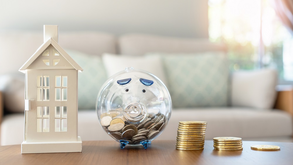 Tirelire transparent en forme de cochon avec de la monnaie et une maquette de maison à côté