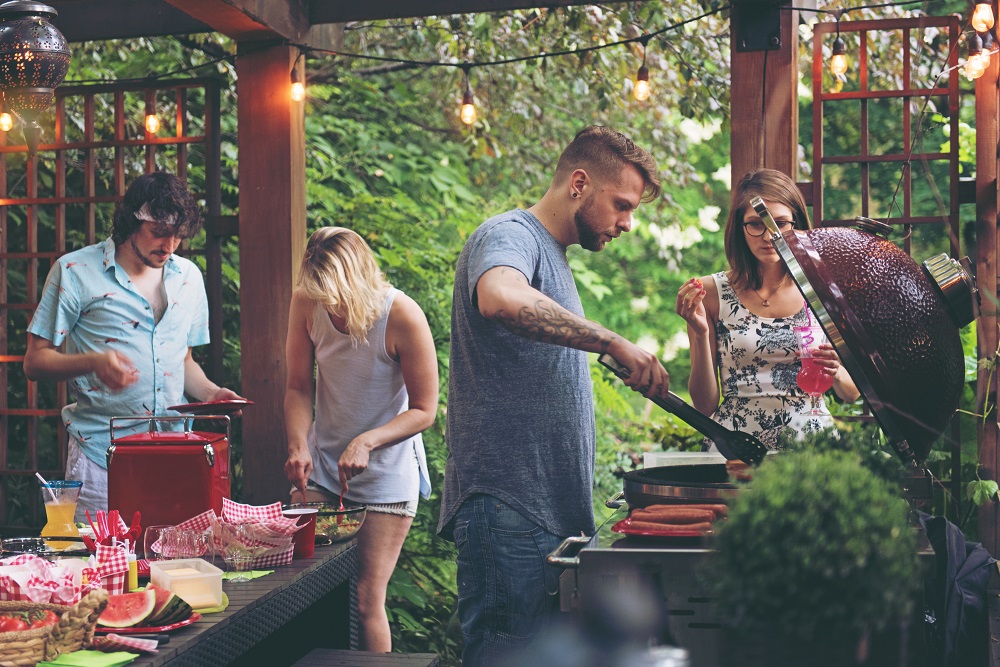 Un groupe d'amis fait de la barbecue dans une cuisine extérieure sous une pergola.