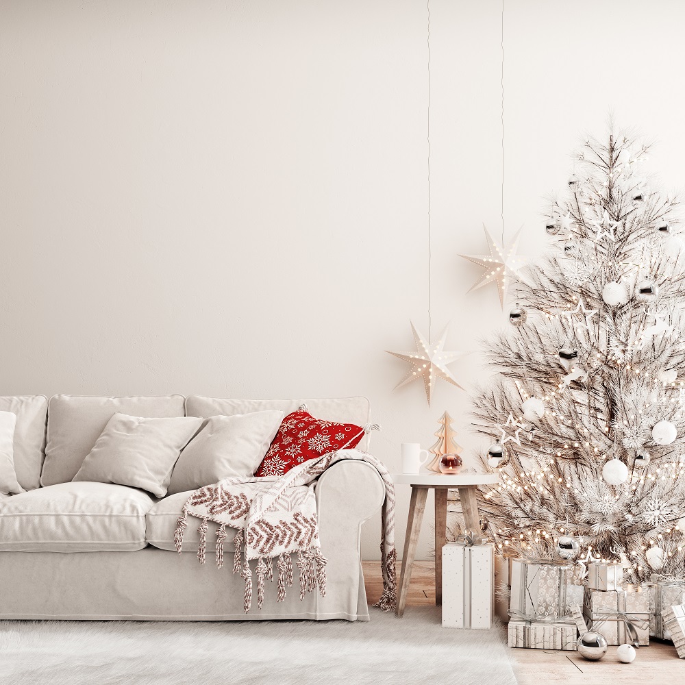 Canapé avec des coussins de Noël et un sapin de Noël décoré en blanc, pour provoquer un coup de cœur lors d'une visite immobilière en hiver. 