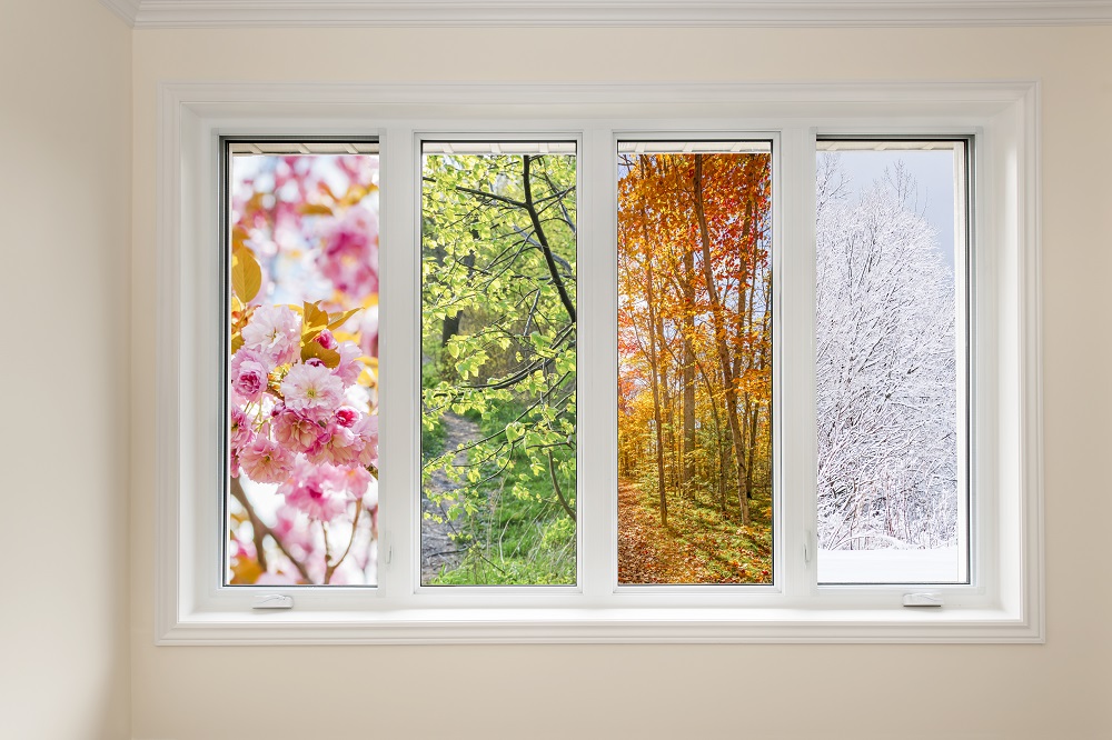 Une fenêtre de l'intérieur d'une maison, partagée en quatre et avec vue des quatre saisons : printemps (fleurs roses), été (arbres verts), automne (forêt automnale), hiver (arbres enneigés.