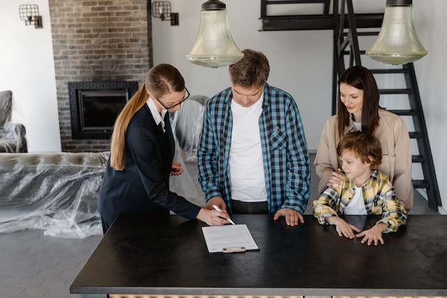 Une professionnelle de l'immobilier fait visiter une maison à vendre rapidement à une famille avec un enfant. 