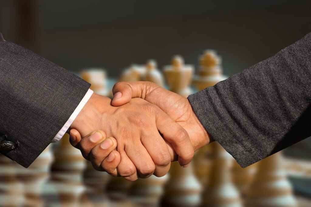 Deux hommes se serrent la main après avoir négocié le prix d'un bien immobilier. En arrière-plan, un jeu d'échecs.