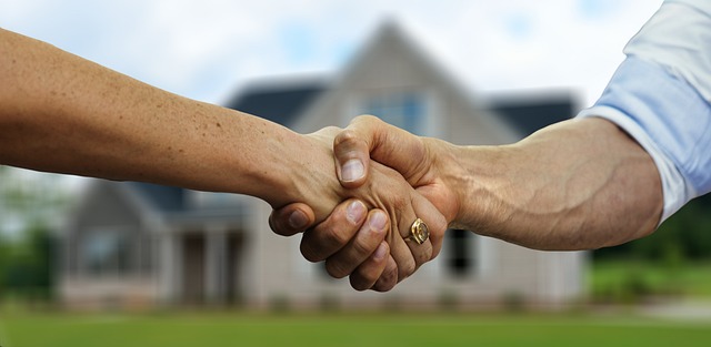 Deux hommes se serrent la main devant une maison à l'occasion de signer une offre d'achat. 